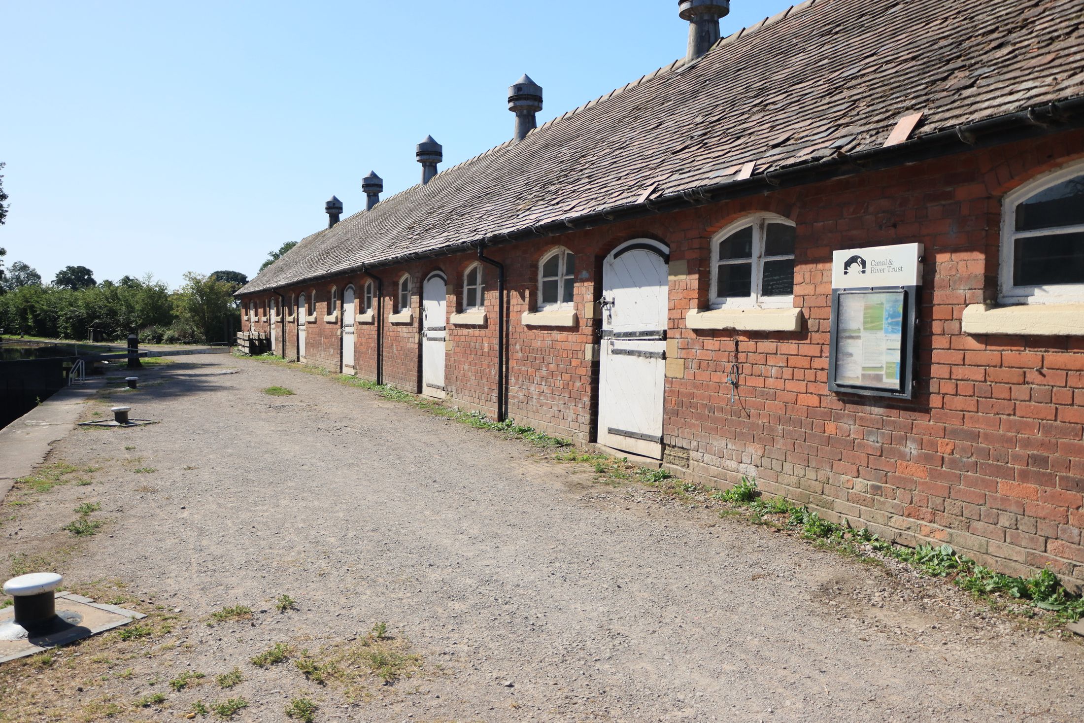 A long historic English stable block with brick walls, white doors and a weathered tiled roof