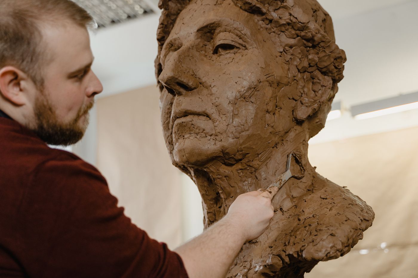 Sculptor working with a loop tool on a large clay portrait bust